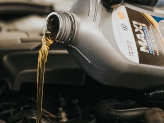Gloved hand pouring engine oil into an engine