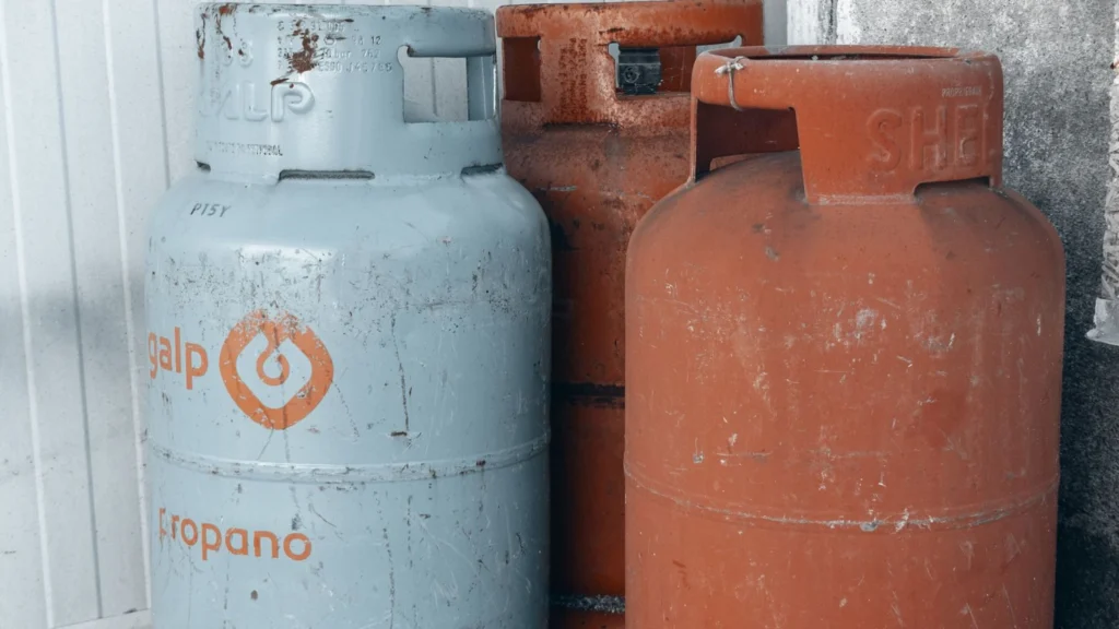 Three propane cylinders standing against a concrete wall