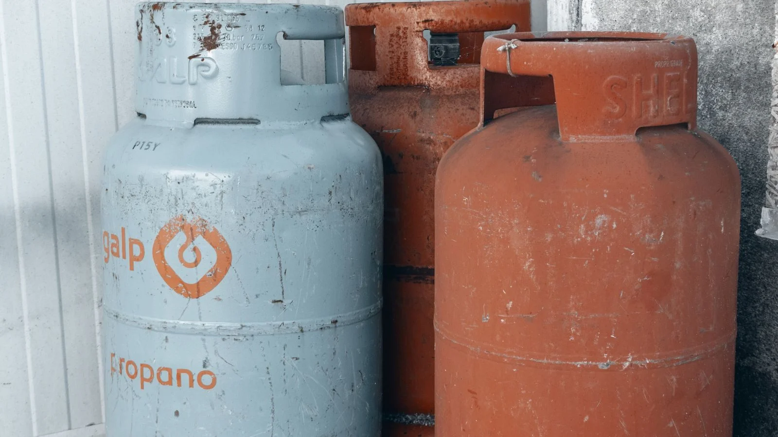 Three propane cylinders standing against a concrete wall