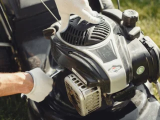 Gloved hands adjusting a lawn mower engine outdoors