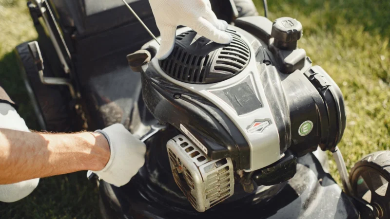 Gloved hands adjusting a lawn mower engine outdoors