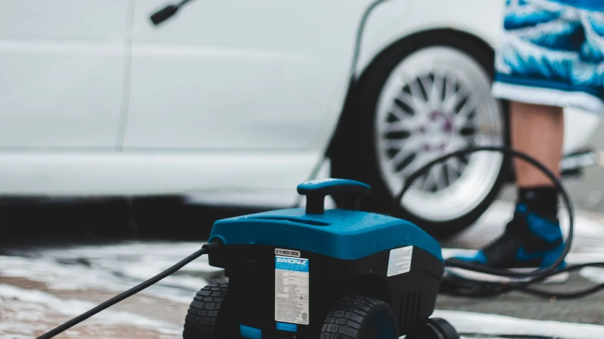 Electric pressure washer standing on a paved driveway beside a car